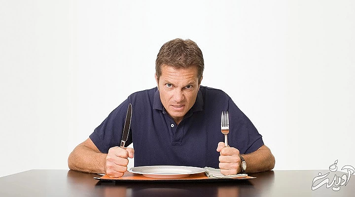 مردی با چهره عصبانی قاشق و چنگال در دست با بشقابی خالی